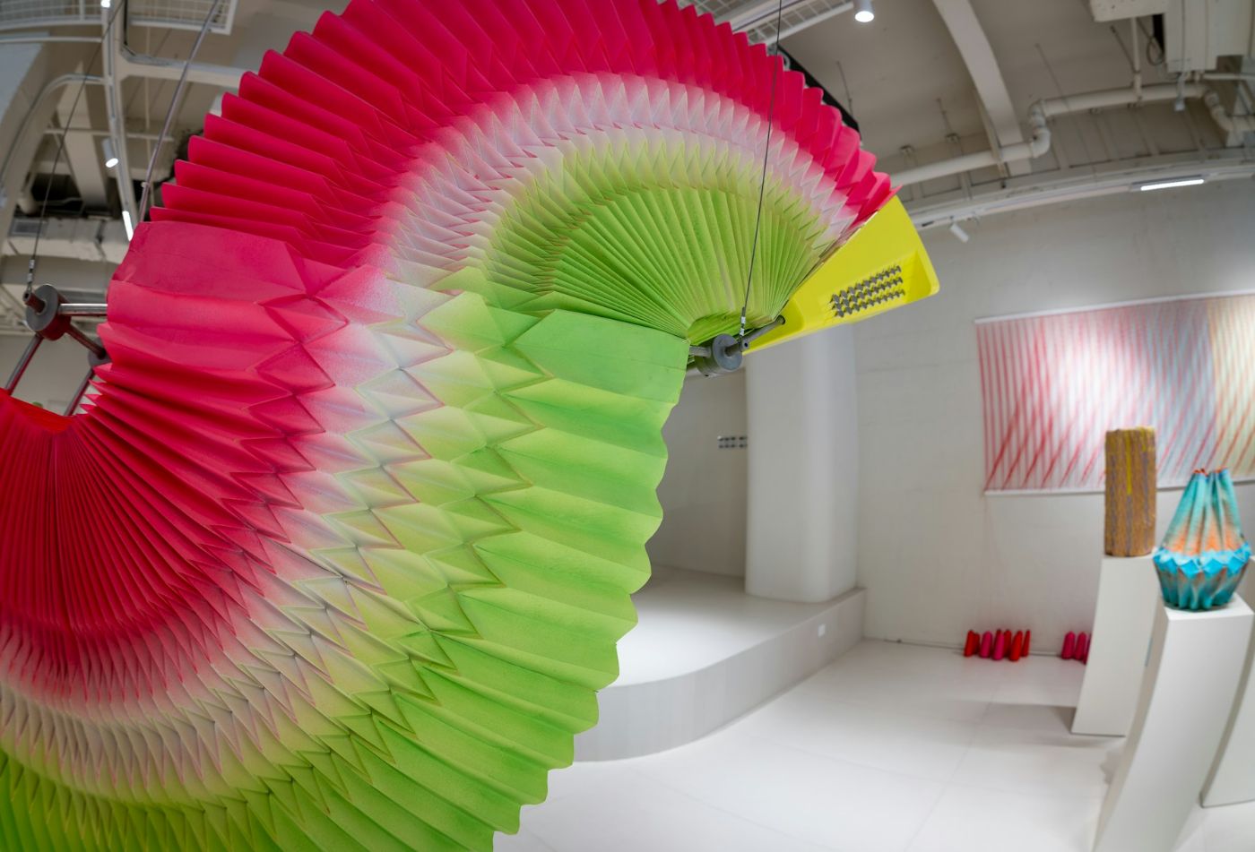 Instalación de papel plegado en degradado de rosa a verde, colgada en una sala blanca
