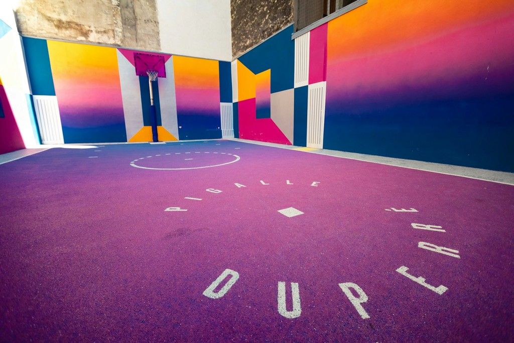 Pista de baloncesto pintada en violeta, rosa y azul entre muros de hormigón
